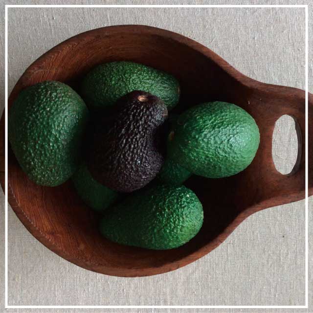 Birds eye view of wooden bowl of fresh avocardos sitting on top of a beige benchtop